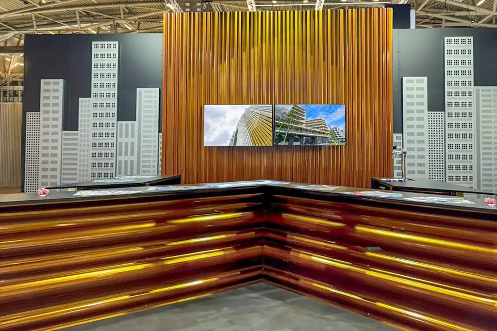 Interiér stánku METROPOLIS od DEKMETAL pro BAU 2025 s unikátním pultem z ohýbané vlny ve tvaru M a perforovanými mrakodrapy a metrem na kazetách DEKCASSETTE